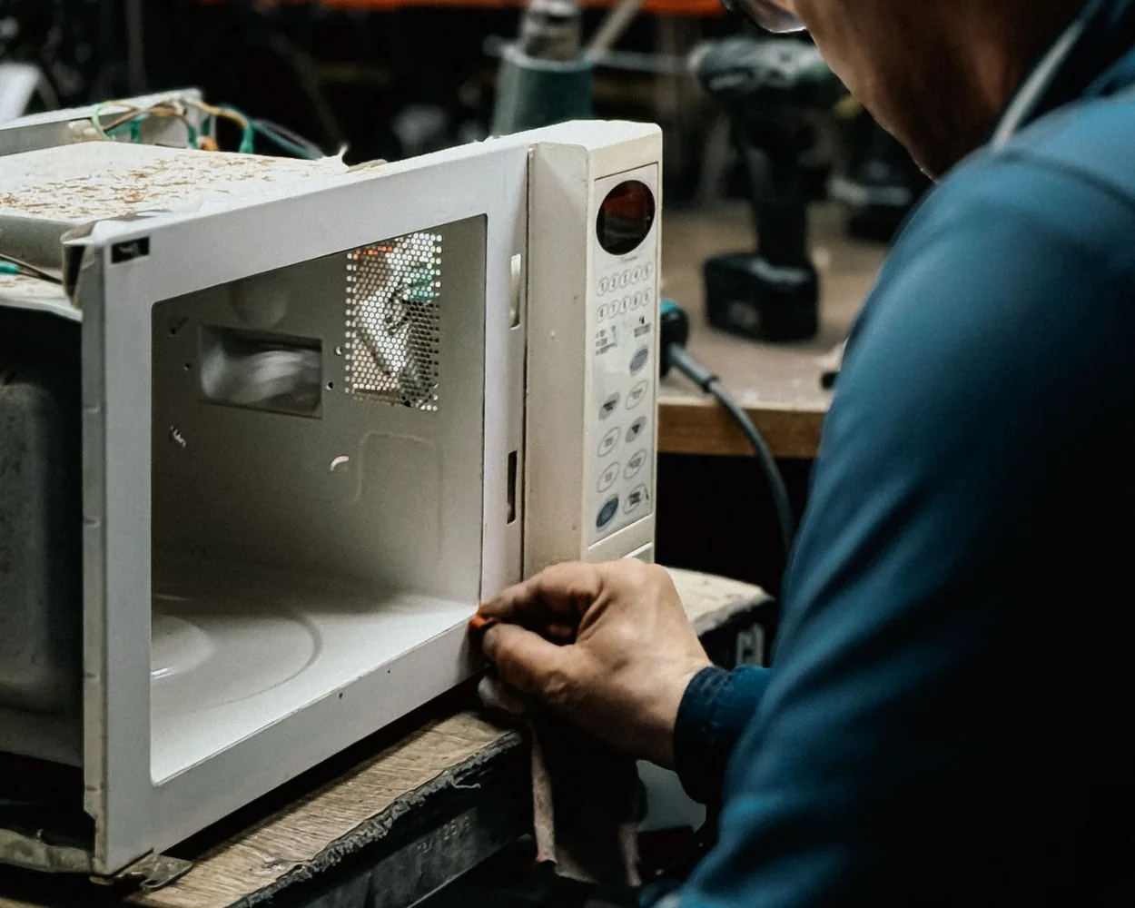 A technician working on an opened microwave oven at a repair bench
