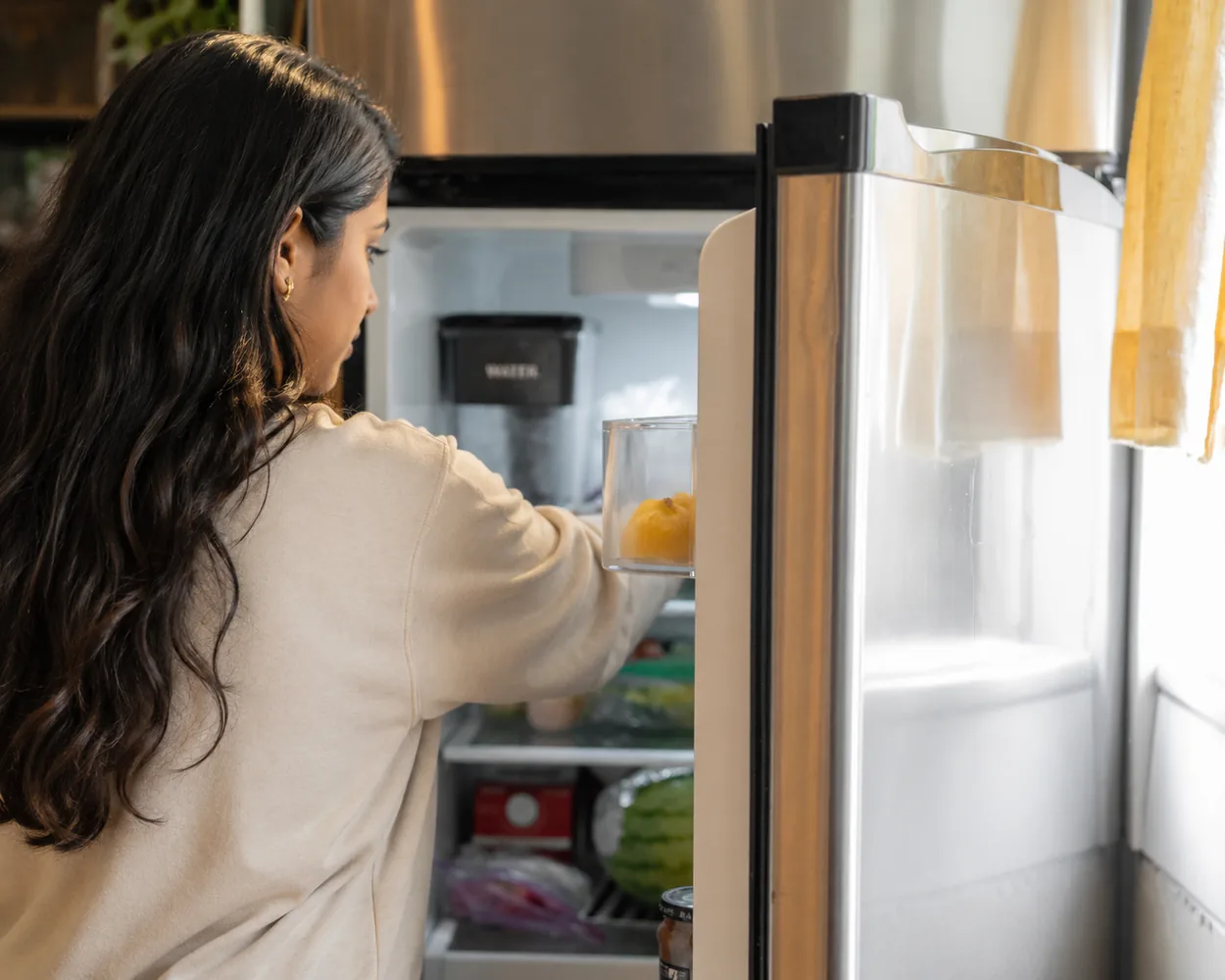 Someone taking food from an open refrigerator in a home kitchen